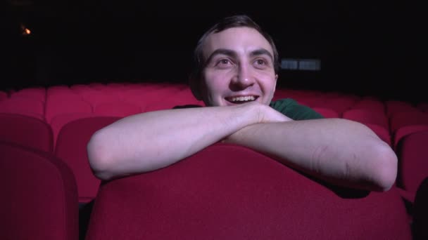 Een man zit in comfortabele rode stoelen in donker cinema theater ziet er komedie en lacht — Stockvideo