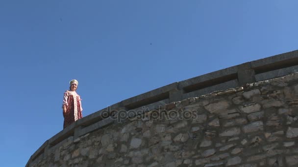 Dívka jde na kamenné zdi, na pozadí oblohy — Stock video
