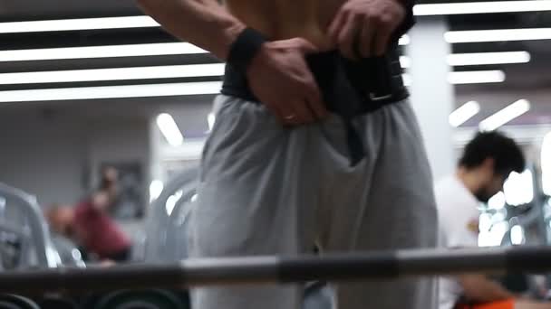Joven culturista se prepara para el ejercicio con una barra en el gimnasio — Vídeos de Stock