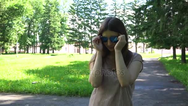 Mujer joven sonriente se pone gafas de sol . — Vídeos de Stock