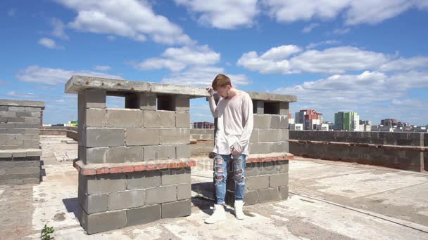 Giovane dai capelli rossi in piedi sul tetto sullo sfondo del paesaggio urbano e cielo blu — Video Stock