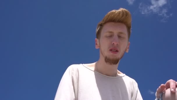 Steadicam-Aufnahme eines jungen rothaarigen, stilvollen Mannes vor klarem blauem Himmel. — Stockvideo