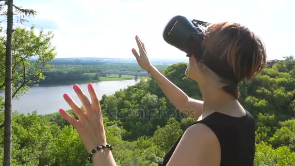 Молодая женщина использует головной дисплей в парке. Игра с использованием VR-шлема для смартфонов — стоковое видео