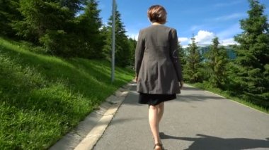 Ağır çekim mutlu gülümseyen genç kadın ceket çevresinde güneşli parkta yaz gününde yürüyüş.