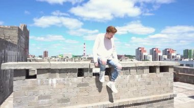 Çatıda bir tuğla duvara genç Kızıl saçlı adam beyaz bir kazak içinde oturur