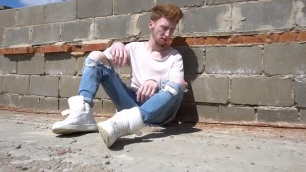 A young red-haired man sits on the roof floor in a hot sunny day — Stock Video