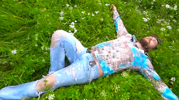 En skjeggete mann ligger på en grønn blomstereng. – stockvideo