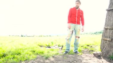 Kırmızı kazak yakışıklı sakallı adam yakınındaki bir alanı ağacında duruyor