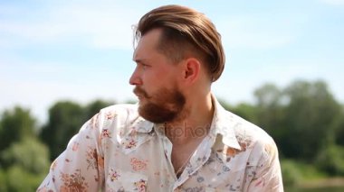 Açık havada kameraya bakarak tişörtlü çekici genç sakallı adam portresi