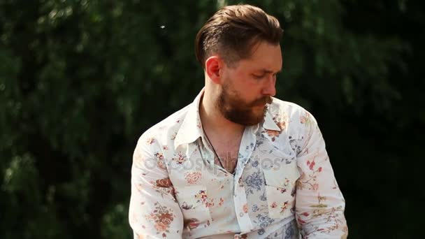 Портрет привлекательного молодого бородатого мужчины в рубашке, смотрящего в камеру на улице — стоковое видео
