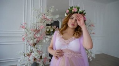Lila sabahlığı ve çiçek baş çelenk hamile güzel genç kadın lüks oda üzerinde yürüyor