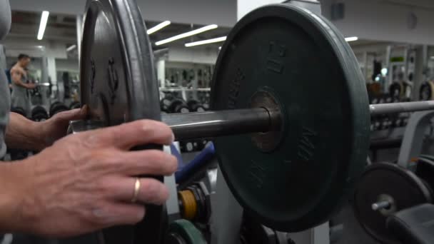 Transición de tiro de hombre musculoso determinado poniendo placas pesadas en la barra y levantamiento en el gimnasio . — Vídeo de stock