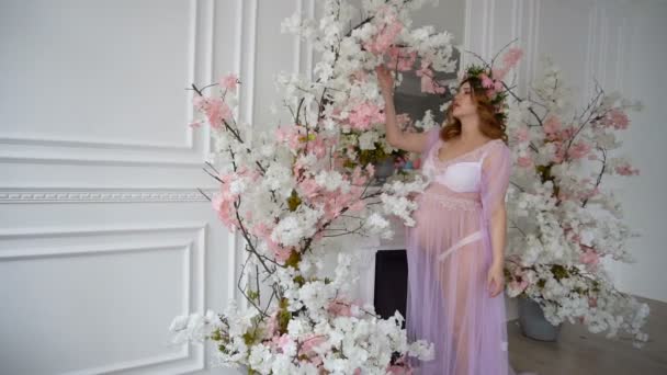 Uma mulher grávida está ao pé da lareira no quarto de luxo, cheirando flores — Vídeo de Stock