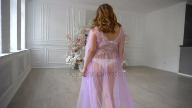 Lila sabahlığı ve çiçek baş çelenk hamile güzel kız lüks oda üzerinde yürüyor