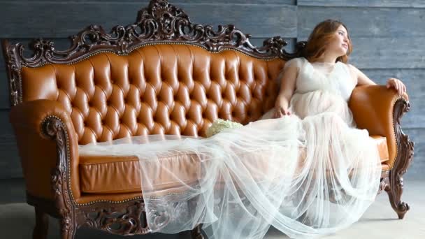 Schwangere junge Braut in luxuriösem Kleid sitzt auf Ledercouch — Stockvideo