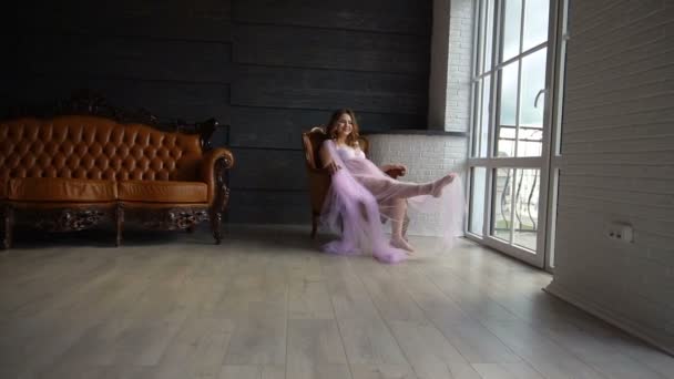 Μια νεαρή έγκυο γυναίκα στο peignoir κάθεται στην καρέκλα — Αρχείο Βίντεο