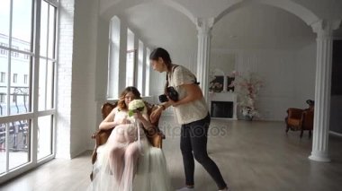Beyaz sabahlığı sandalyede oturan ve fotoğrafçı için poz güzel genç hamile kadın