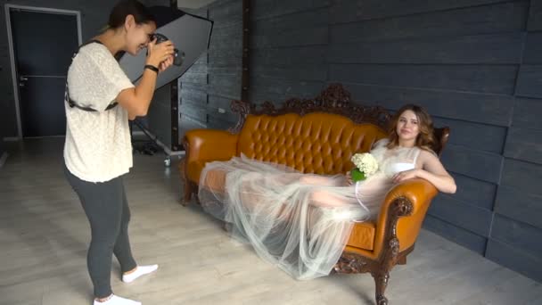 Krásný model těhotná dívka v bílých šatech nebo peignoir na trenéra pózování pro fotografa — Stock video