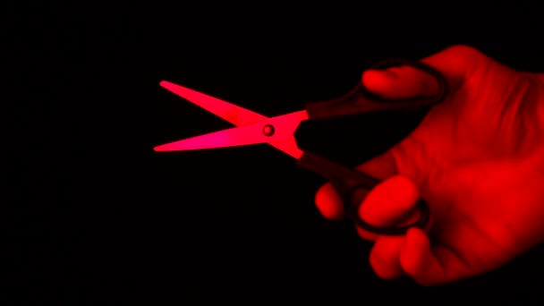 Schere in der Hand in rotem Licht isoliert auf schwarzem Hintergrund — Stockvideo