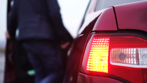 Az ember beszáll a kocsiba. A sofőr kinyitja a piros autó ajtaját és a volán mögött ül. — Stock videók