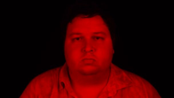 Porträtaufnahme mit roter Beleuchtung: Dicker Mann steht isoliert auf schwarzem Hintergrund und blickt in die Kamera — Stockvideo