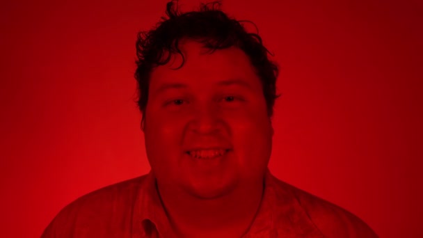 Χοντρός άντρας στέκεται πίσω από κόκκινα φώτα νέον χαμογελώντας και κοιτάζοντας την κάμερα — Αρχείο Βίντεο