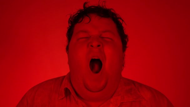ヨーロッパの男があくびをし、口を開けて疲れました。赤い照明だハンサムな男したい眠りにカメラに赤の背景 — ストック動画