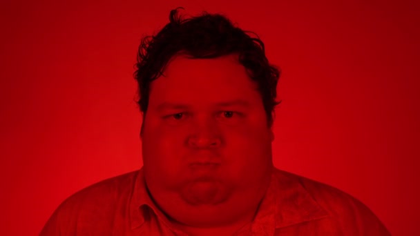 Fiatalember áll a piros világítás szoba és puffadt arc vicces vagy dühös arcát. Levegővel felfújt száj. — Stock videók