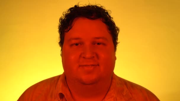 Retrato fotografiado con luz roja: Hombre gordo parado aislado sobre fondo amarillo y sonriendo mientras mira a la cámara — Vídeos de Stock