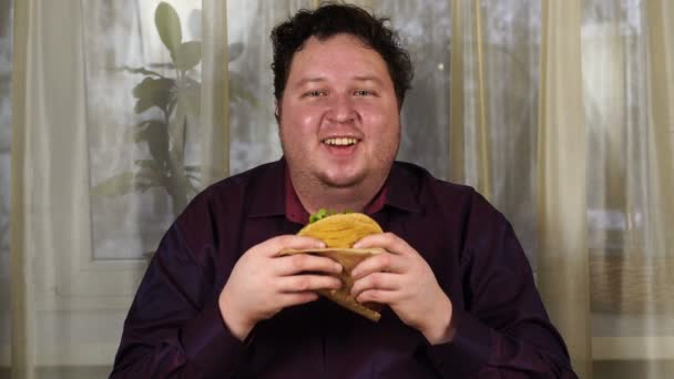 Young man holding a sandwich. Fat guy eats fast food. Tortilla is not helpful food. Very hungry guy. — 图库视频影像