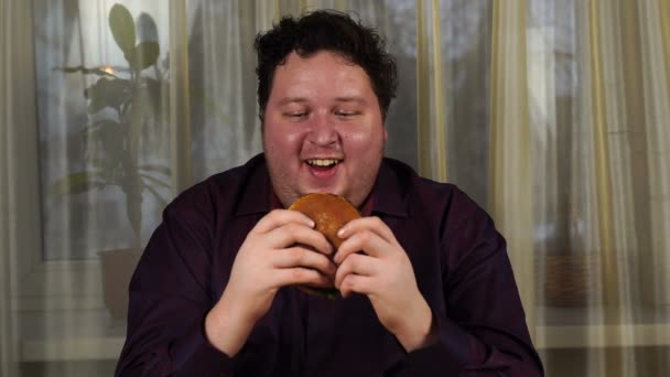 Young man holding a hamburger. Fat guy eats fast food. Burger is not helpful food. Very hungry guy. — 图库视频影像