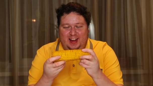 Young man eating boiled corn at home. — Stock Video