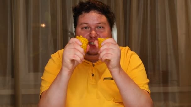 Young man eating boiled corn at home. — Stockvideo