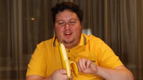 Giovane uomo grasso mangiare banana a casa — Video Stock