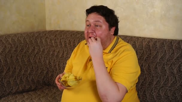 Mann mit Schüssel Kartoffelchips vor dem Fernseher auf Sofa im Wohnzimmer — Stockvideo