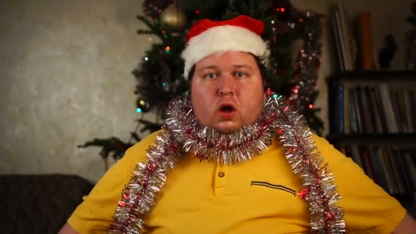 Man in Santa hat and tinsel sitting with open mouth — Stock Video