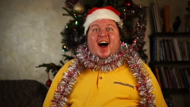 Muž v klobouku Santa a tinsel sedí s šokovanými a překvapenými emocemi — Stock video
