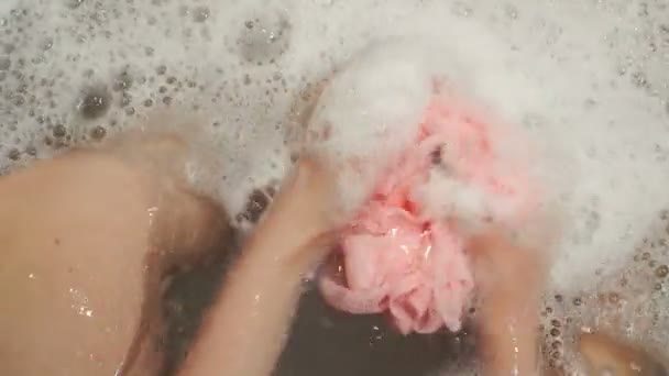 Female hand holds pink washcloth with soap foam at bath — Stock Video