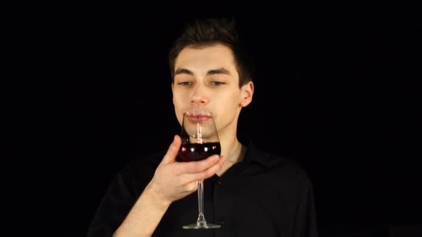 Mann schüttelt das Glas Wein und probiert es auf schwarzem Hintergrund — Stockvideo