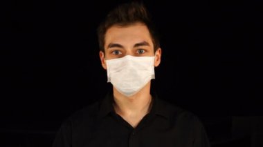 Siyah üzerine izole edilmiş koruyucu tıbbi maske takan genç bir adamın portresi. Salgın