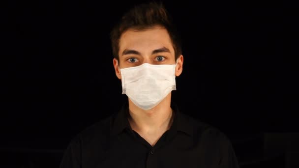 Ritratto di un giovane uomo che indossa una maschera medica protettiva isolata sul nero. Pandemia — Video Stock
