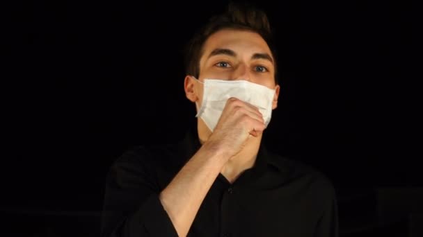 Young man in medical mask sneezes or coughing, isolated on black — Stock Video