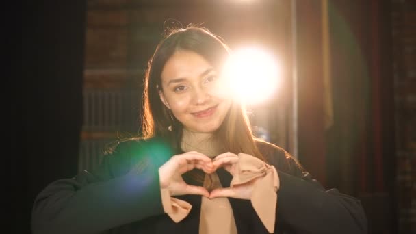 Mooi meisje is het maken van een hart vorm symbool met haar vingers. Ze lacht omdat ze van je houdt. — Stockvideo
