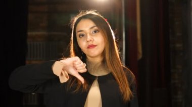 Ciddi, güzel bir genç kadın baş parmağını aşağı gösteriyor.