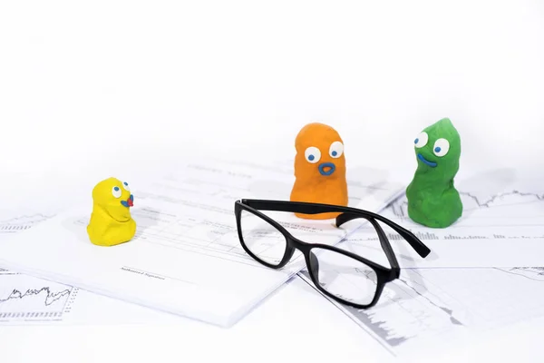 Funny figures made from Play Clay on white documents with glasses. — Stock Photo, Image