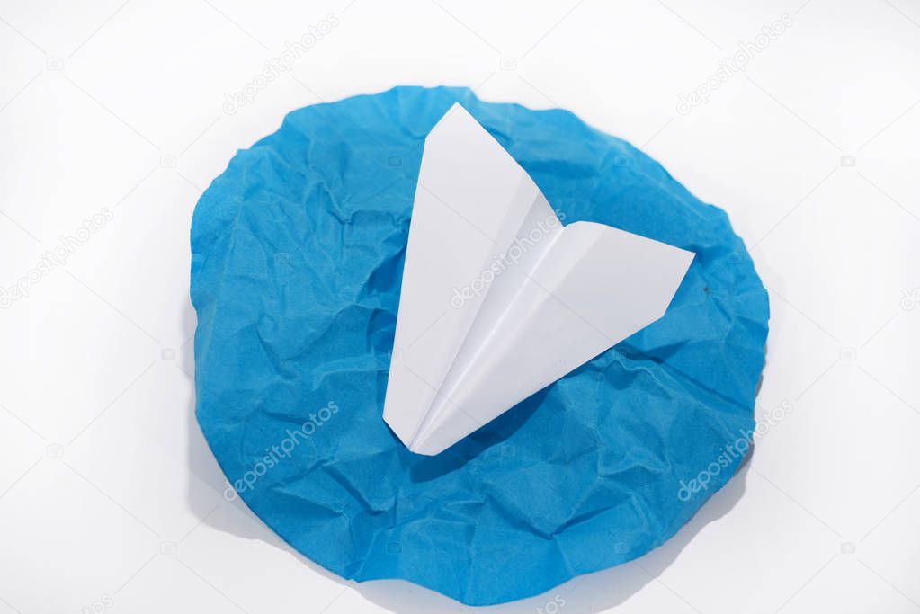 White paper plane on round blue circle. Abstract photo.