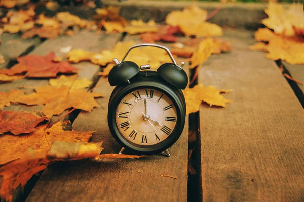 Foto in stile retrò. Vintage sveglia nera su foglie autunnali. Il tempo cambia foto astratta. Ora legale . — Foto Stock