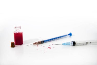 İlaç şırıngası ve beyaz masadaki cam tüpten kırmızı damlalar. Virüs soyut fotoğrafı.