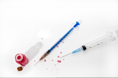 İlaç şırıngası ve beyaz masadaki cam tüpten kırmızı damlalar. Virüs soyut fotoğrafı.