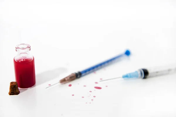 Strzykawka medyczna i czerwone krople ze szklanej tuby na białym stole. Wirus abstrakcyjne zdjęcie. — Zdjęcie stockowe